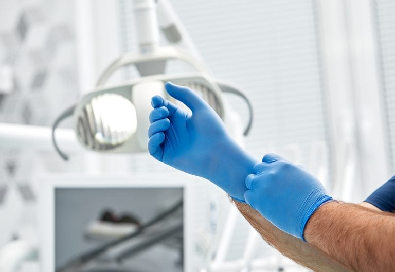 A female dentist puts on gloves against a background of dental equipment in a dental office. Happy patient and dentist concept