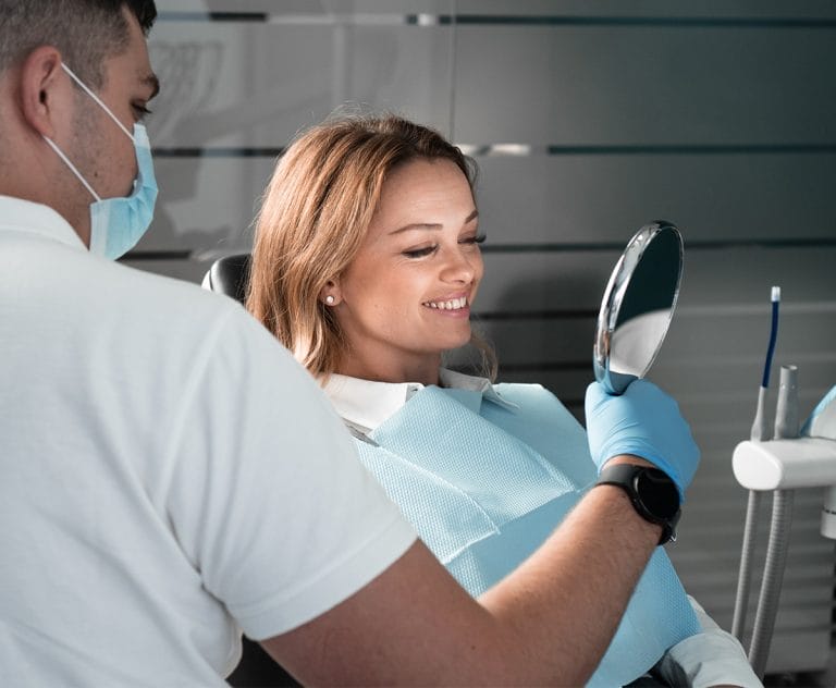 Smiling and happy woman in dental clinic satisfied with the result of dentist's work. The dentist shows the patient the condition of her oral cavity with the help mirror. Looking at herself in mirror. High quality photo